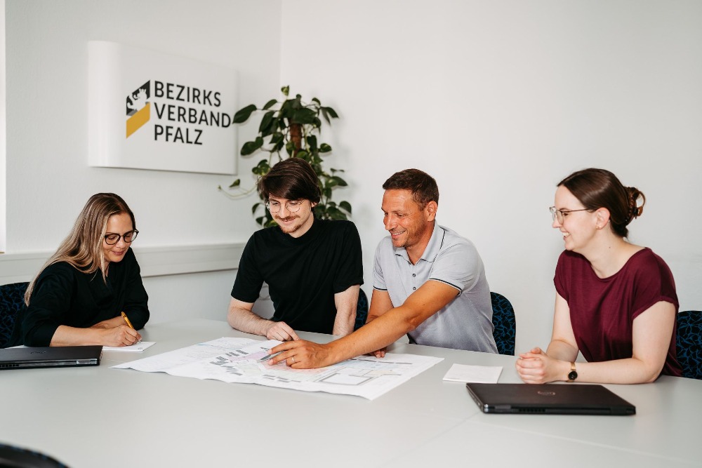 Vier Menschen sitzen gemeinsam an einem Tisch und besprechen einen Bauplan 